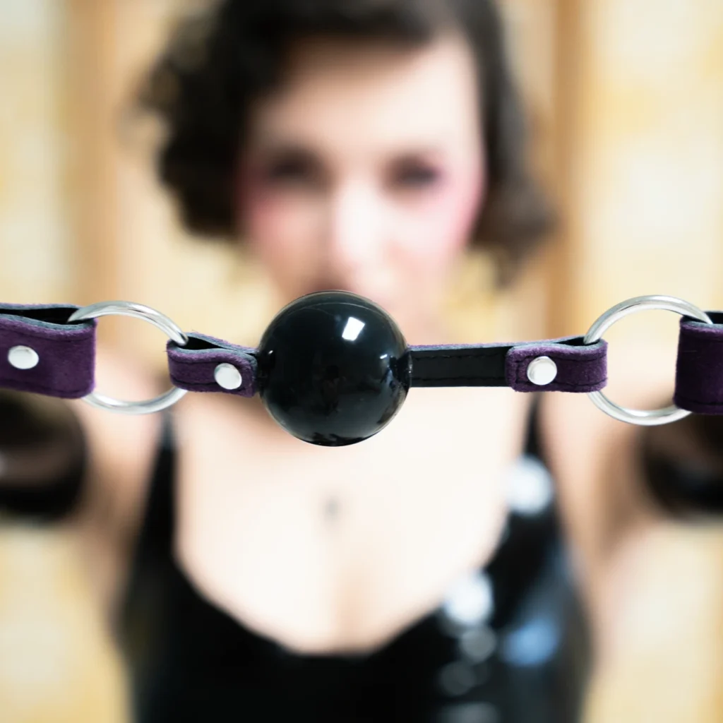 Close-up portrait of Mistress Obelia with a gag ball in soft focus