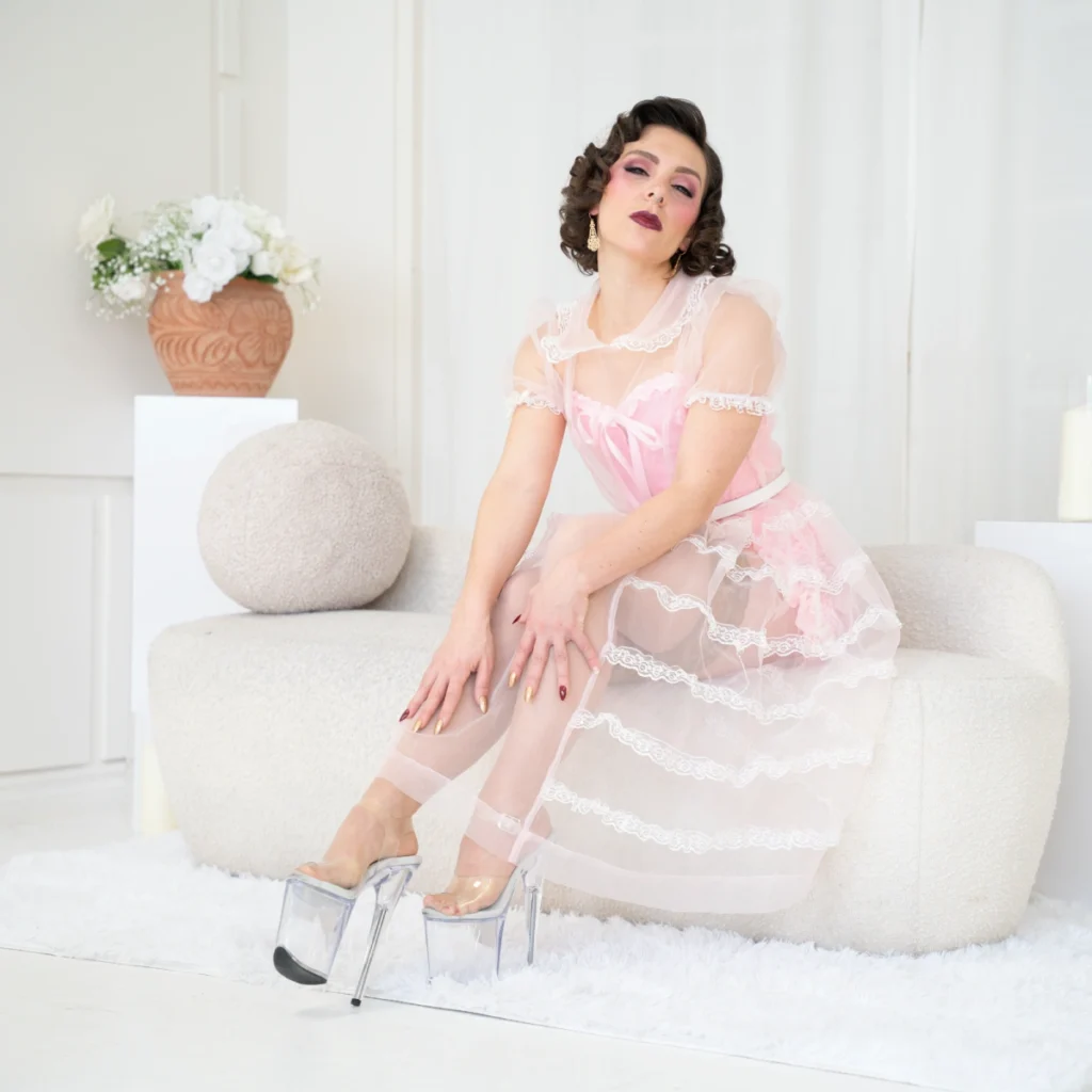 Mistress Obelia in a white room wearing an elegant dress and a pink corset