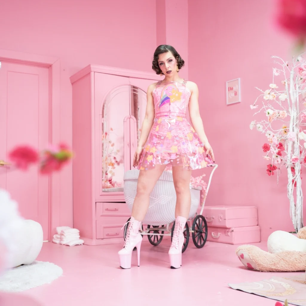 Mistress Obelia standing in a pink room with diapers in the background